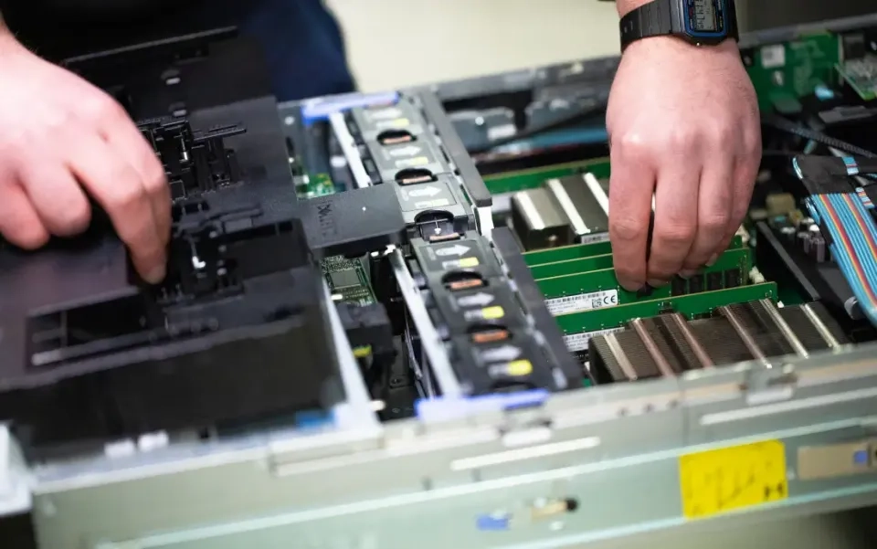 Nahaufnahme der Hände einer Person, die Computerkomponenten in einem Server oder Desktop-Computer installiert oder anpasst, mit sichtbaren Speichermodulen, Leiterplatten und Kabeln.