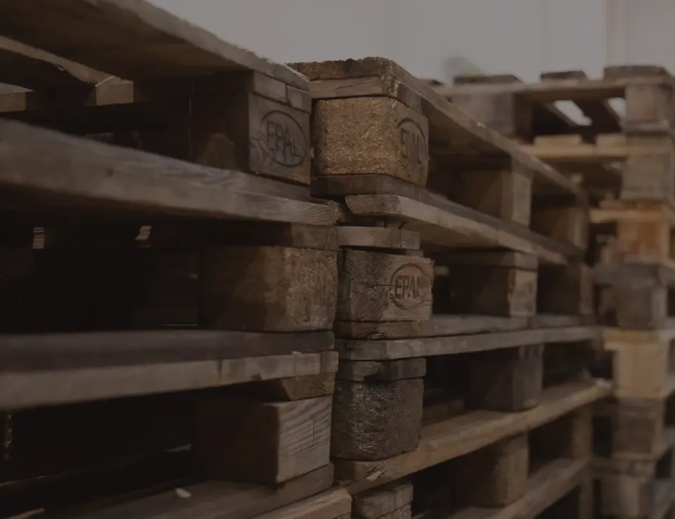 Eine Nahaufnahme von in Reihen gestapelten Holzpaletten in einem Lagerhaus, die die Struktur und Abnutzung des Holzes zeigt.
