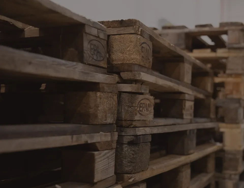 Eine Nahaufnahme gestapelter Holzpaletten in einem Lagerhaus oder Lagerbereich. Man sieht ihre verwitterte Struktur und das auf die Seitenblöcke geprägte EPAL-Logo.