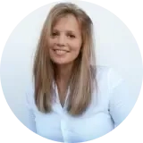 Eine Frau mit langen blonden Haaren und einem weißen Hemd mit Knöpfen lächelt vor einem schlichten weißen Hintergrund.