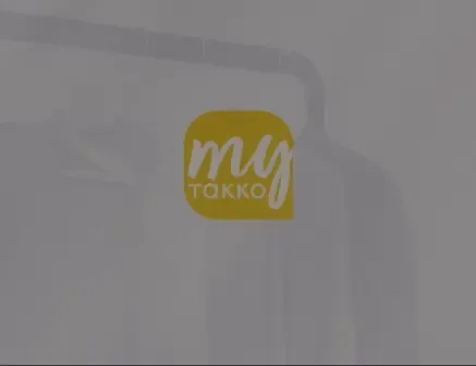 Ein gelbes quadratisches Logo mit den Worten „my TAKKO“ in weißer Schrift, überlagert auf einem unscharfen Hintergrund, der weiße Kleidung auf Kleiderbügeln zeigt.
