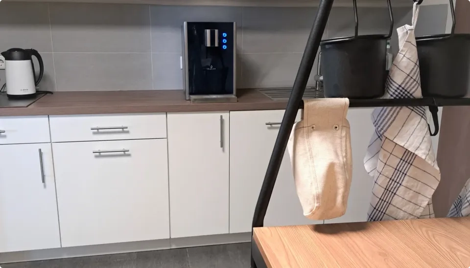 Eine moderne Küche verfügt über weiße Schränke, eine Holzarbeitsplatte, eine schwarze Kaffeemaschine, einen weißen Wasserkocher und ein kariertes Geschirrtuch, das neben einer beigen Stofftasche an einem Metallgestell hängt.