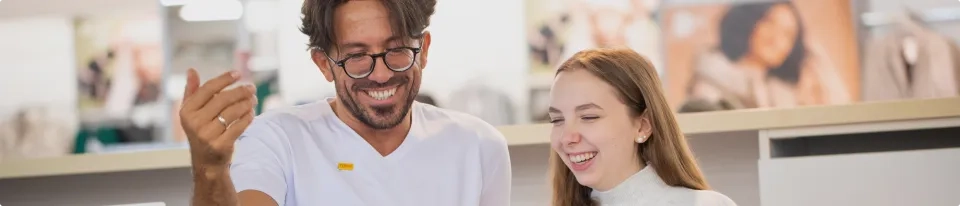 Ein Mann und eine Frau lächeln und lachen zusammen in einem Innenbereich und stehen vor einem unscharfen Hintergrund mit sanften Farben und unscharfen Bildern.