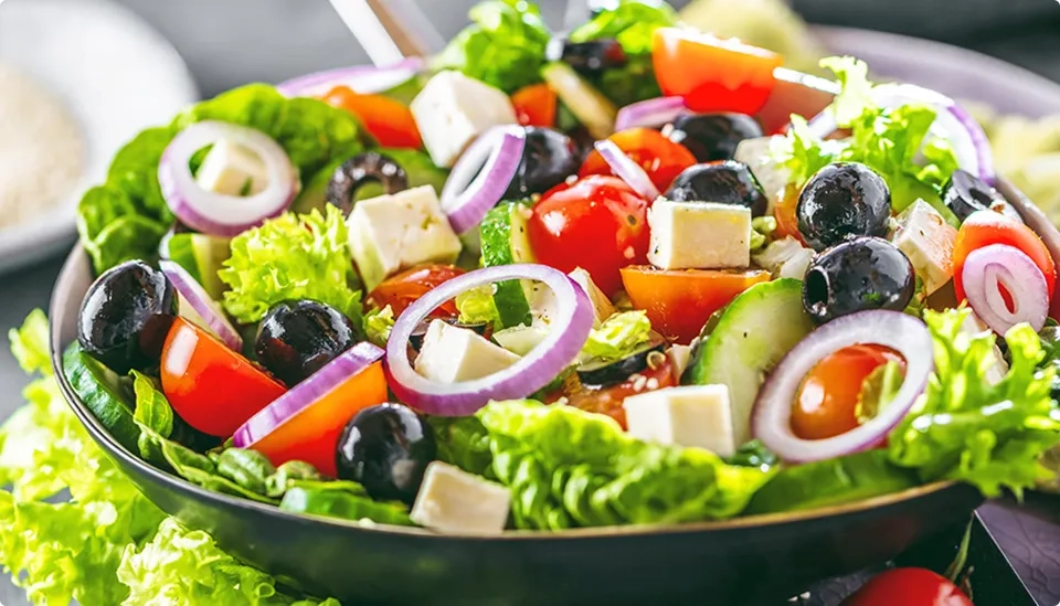 A fresh Greek salad with lettuce, cherry tomatoes, cucumber, red onion rings, black olives, and feta cheese cubes in a bowl.
