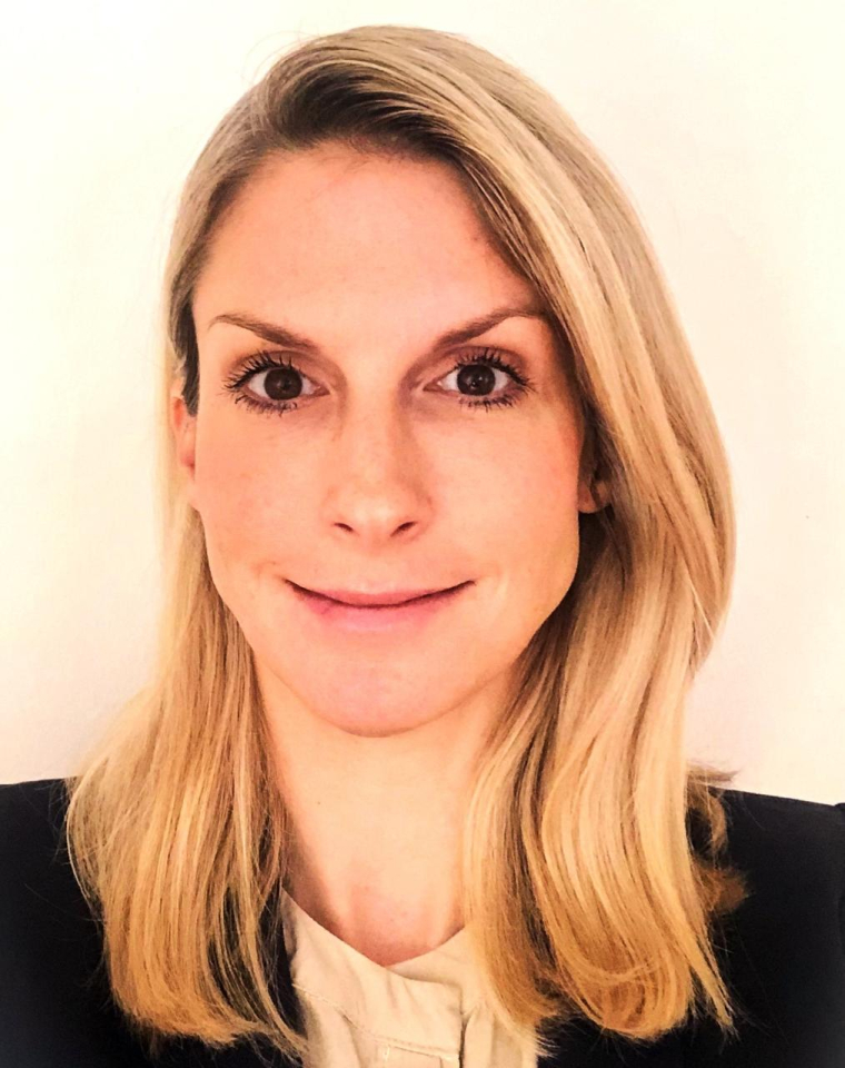 A woman with straight, shoulder-length blonde hair is smiling slightly at the camera. She is wearing a light-coloured top and a dark blazer, with a plain white background behind her.